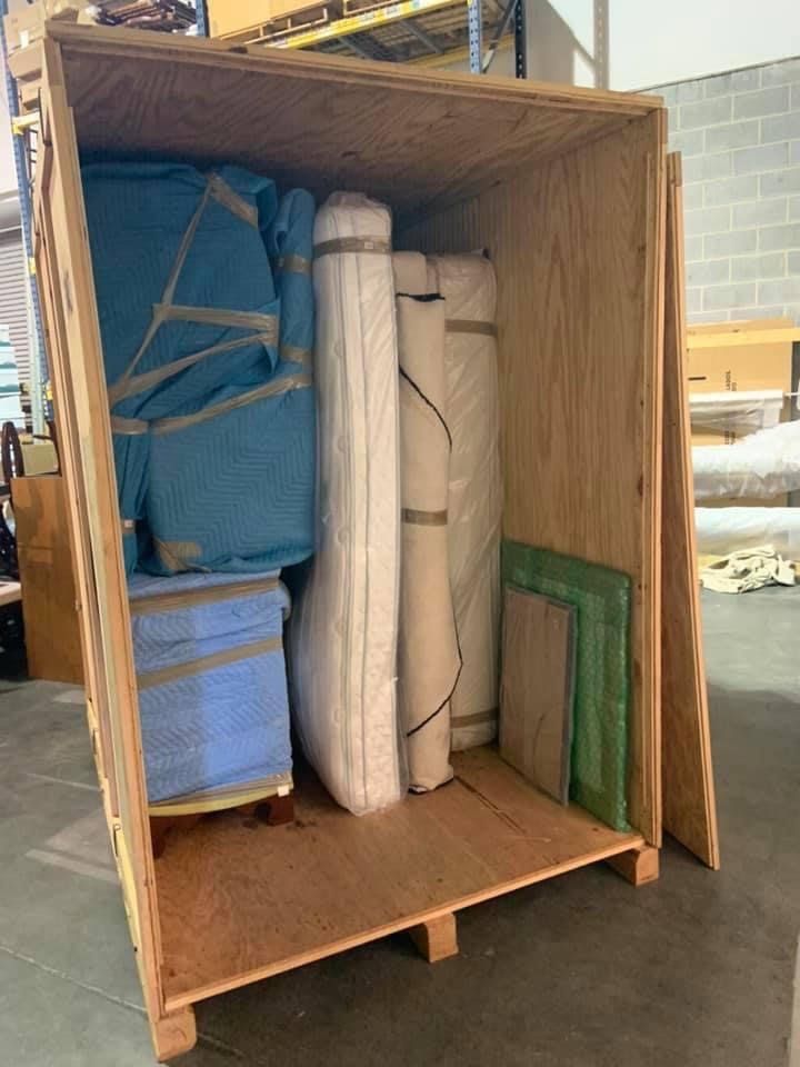 Open wooden crate packed with rolled and boxed materials in a warehouse.