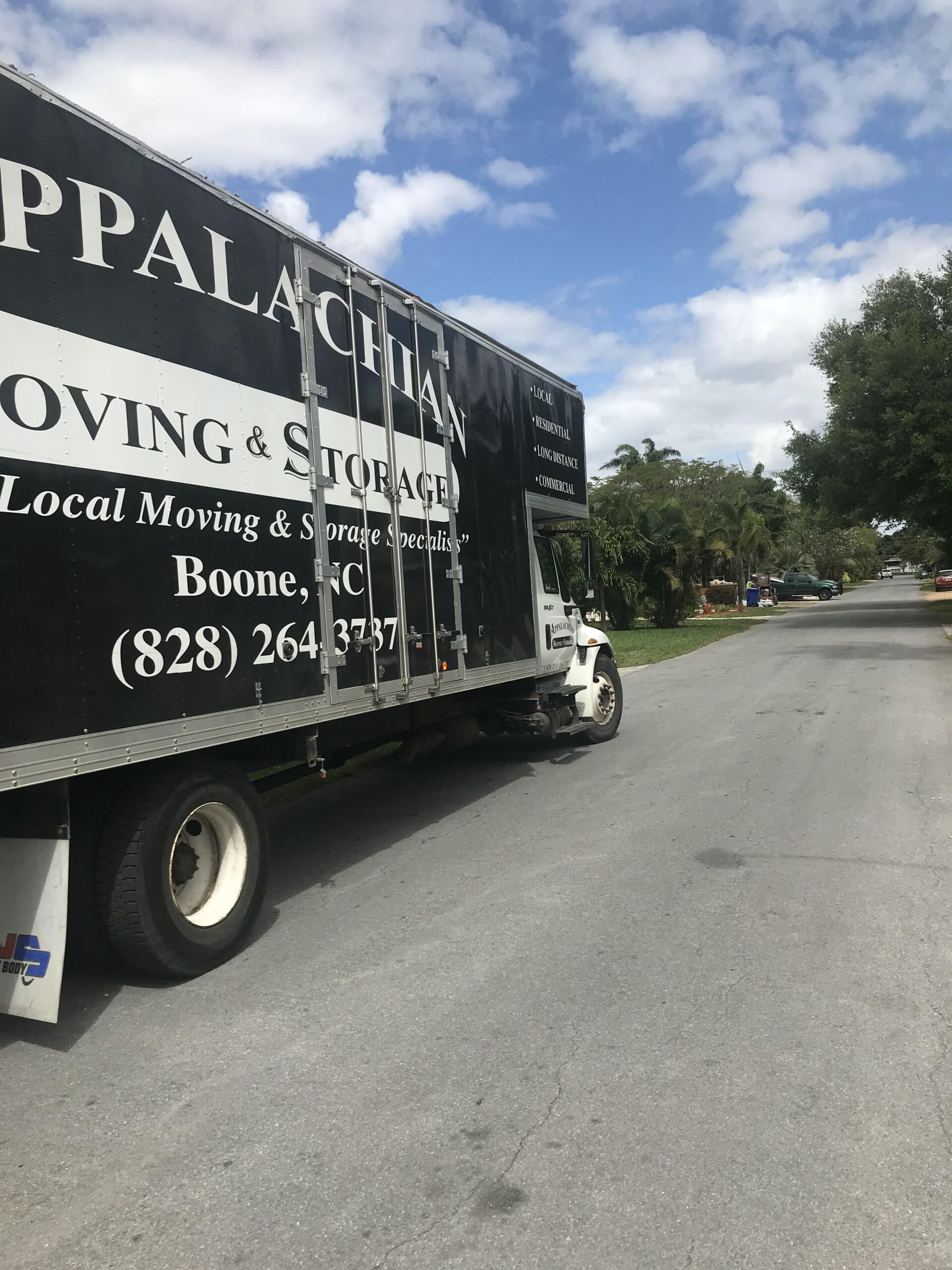 Delivery service worker loading truck - Deep Gap, NC - Appalachian Moving & Storage Black moving truck on a quiet suburban street under a partly cloudy sky.