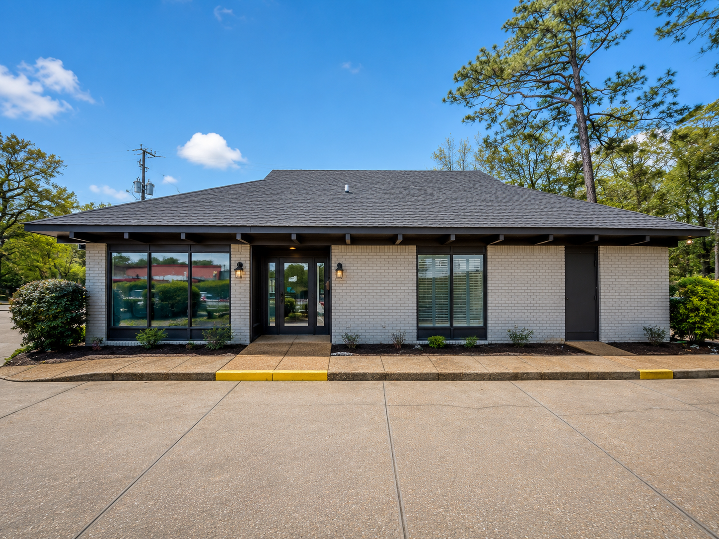 Single-story brick office building with dark roof, large windows, and a yellow curb under a blue sky