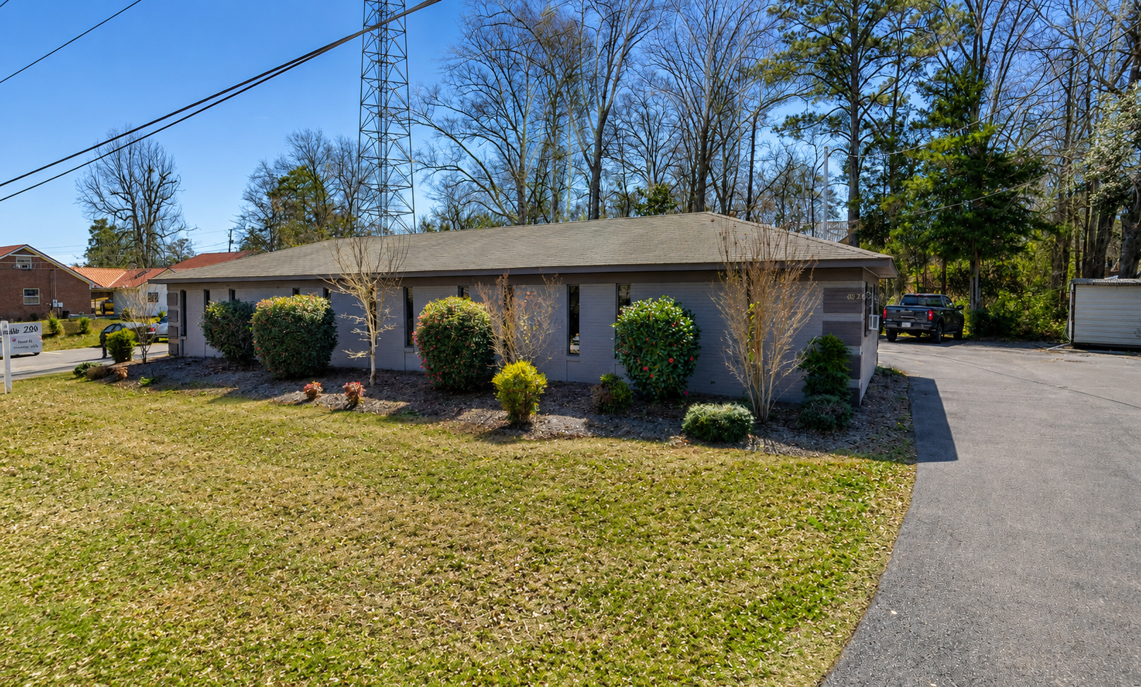 Single-story brick house with a gray roof, front lawn, shrubs, and a driveway on a sunny day