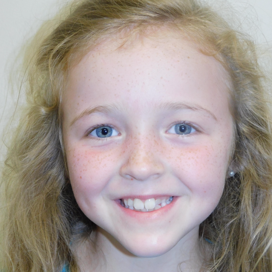 A person with long blonde hair and blue eyes smiling at the camera against a plain background.