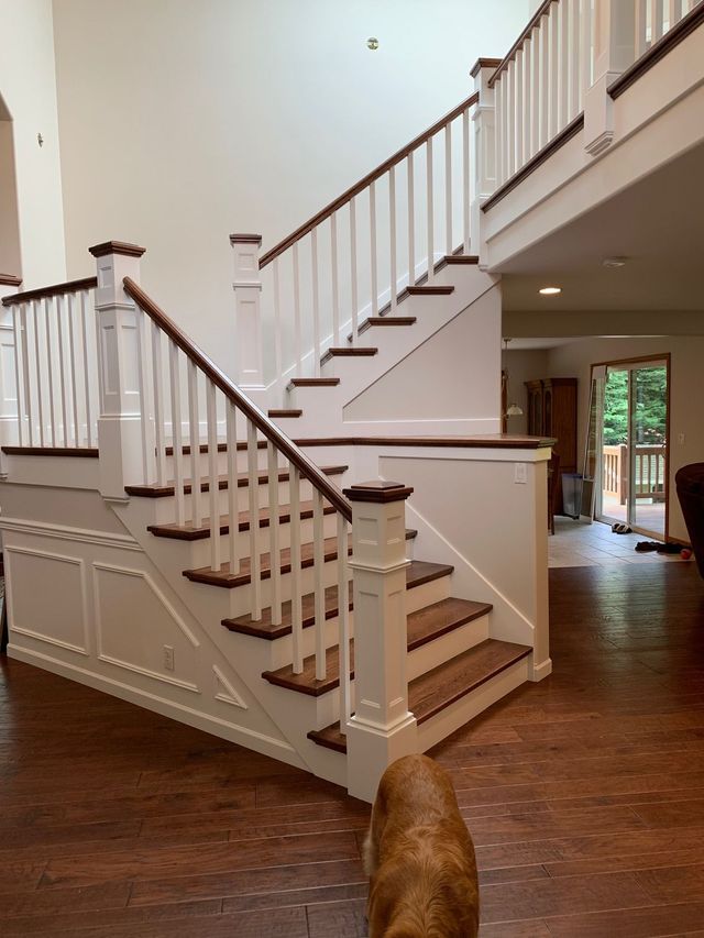Staircase with white balusters, a stained wood handrail and a paneled newel post