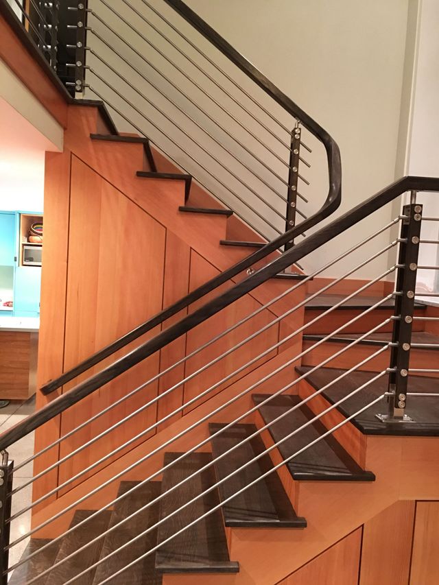 Horizontal metal bar railing with a dark handrail beside a wood-paneled staircase