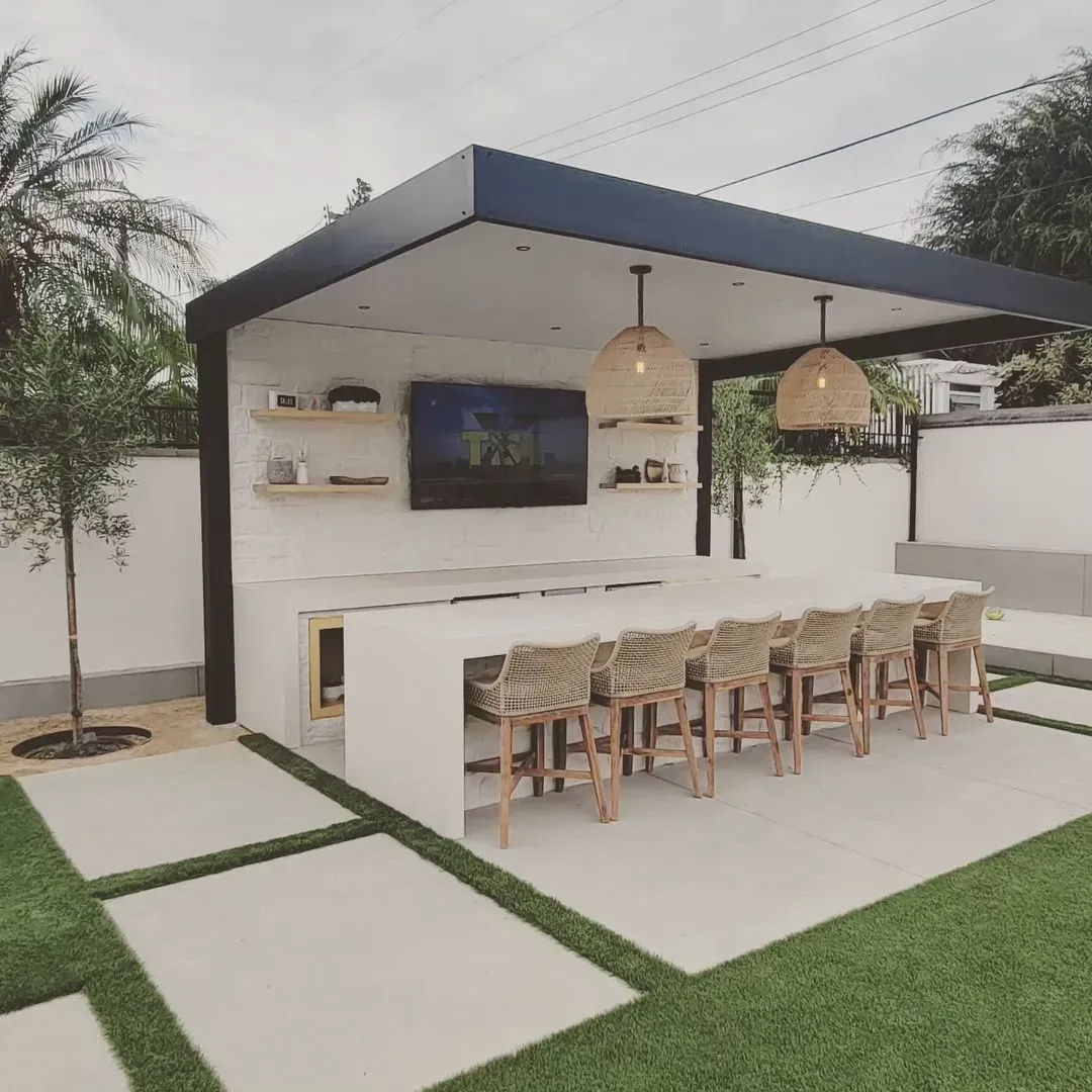 Outdoor bar with a white countertop, stools, TV, and overhead lighting.