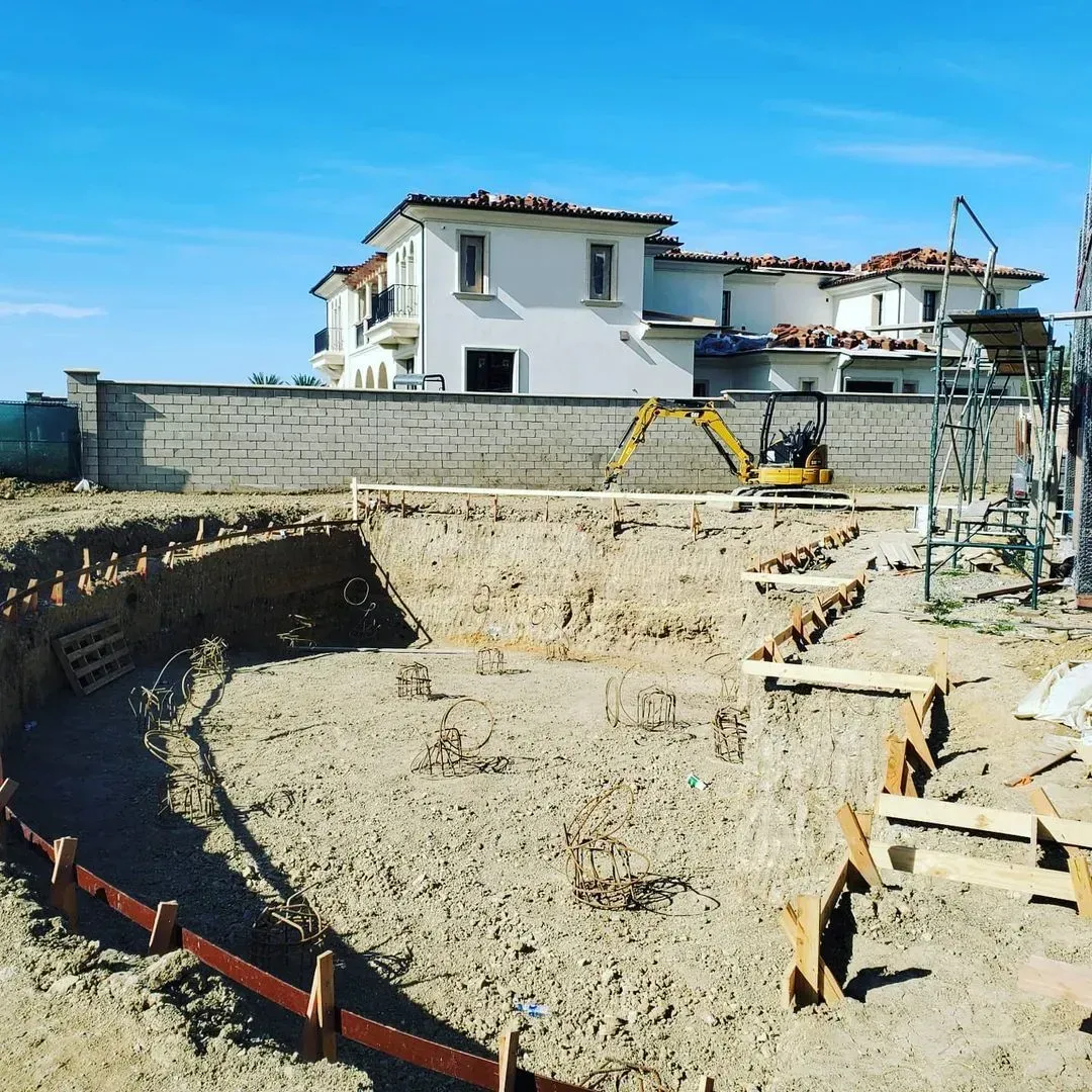 Pool construction site; excavator in pit with house in background on a sunny day.