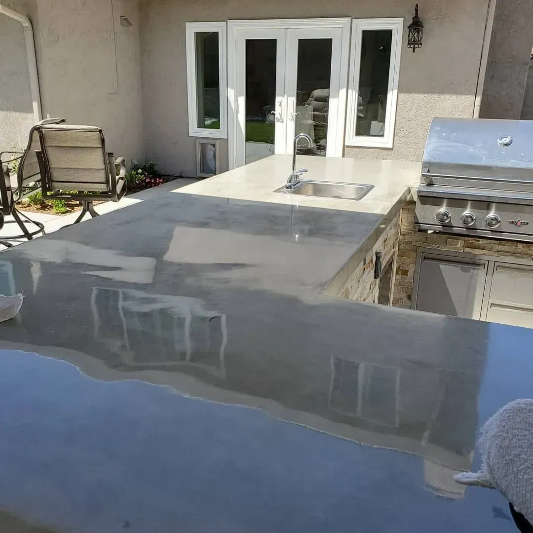 Outdoor concrete countertop with a sink and a built-in grill near a house with glass doors.