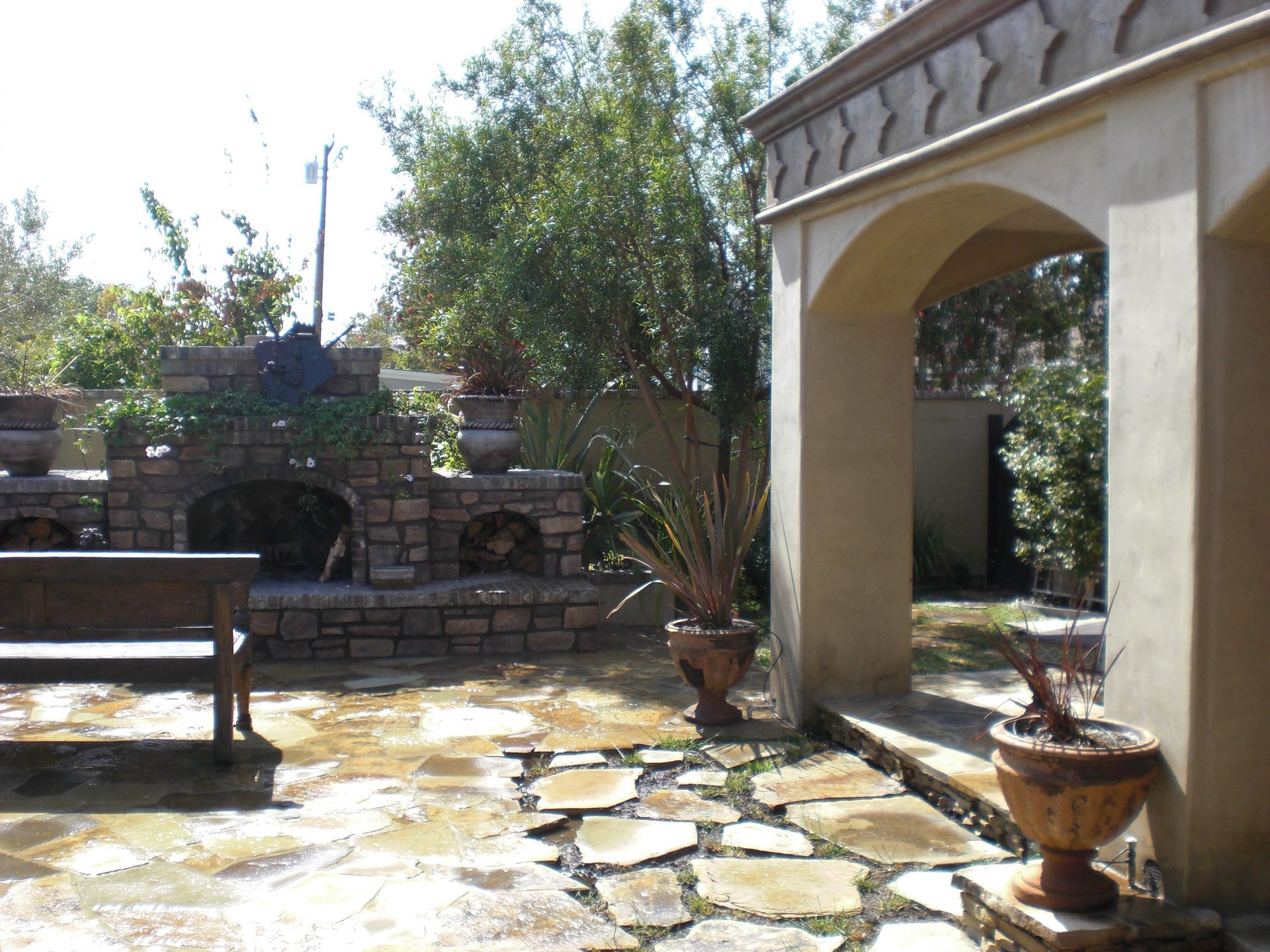 Stone patio with arched entry, fireplace, bench, and potted plants.