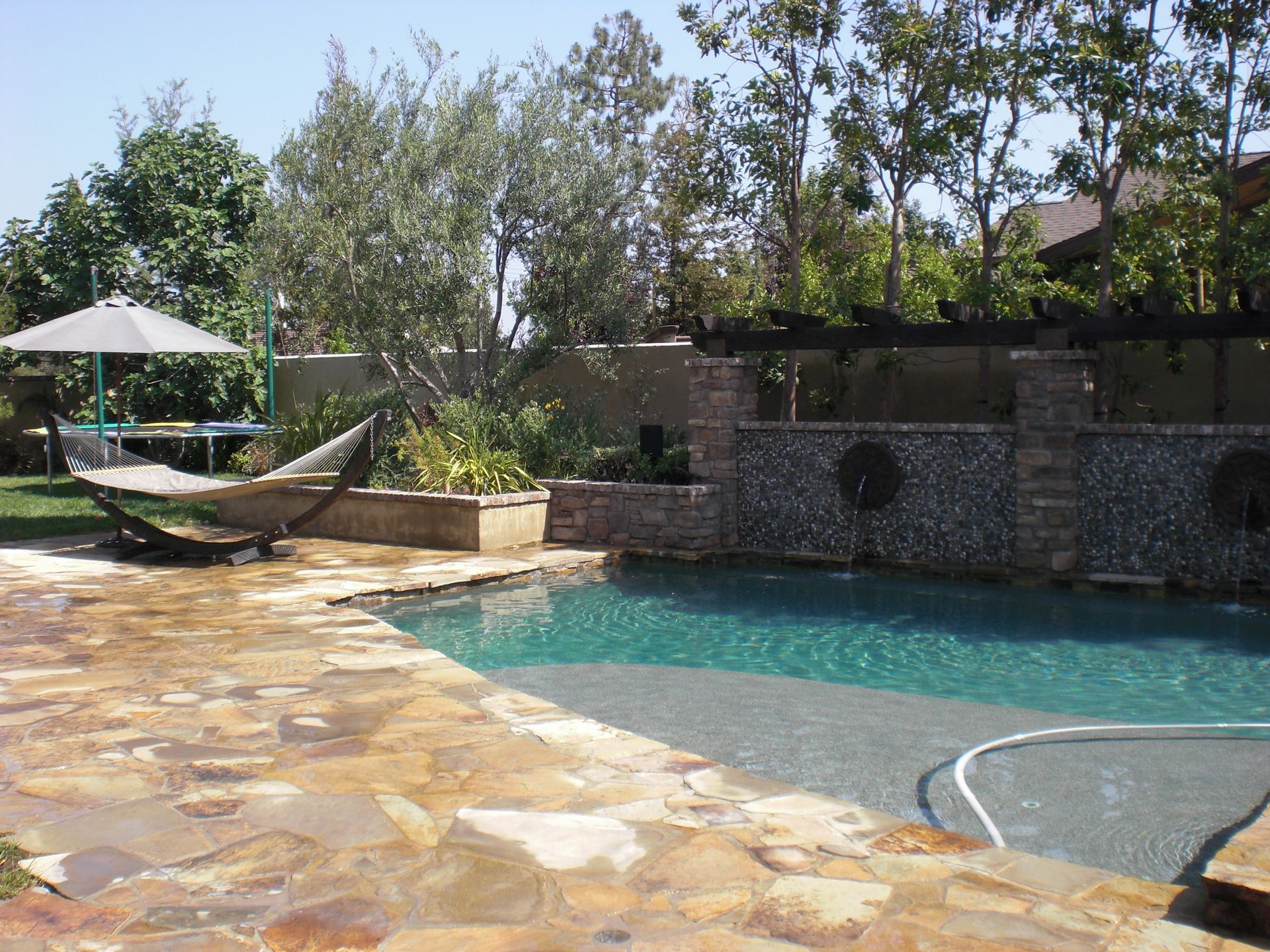 Swimming pool with stone deck, hammock, and waterfall feature.