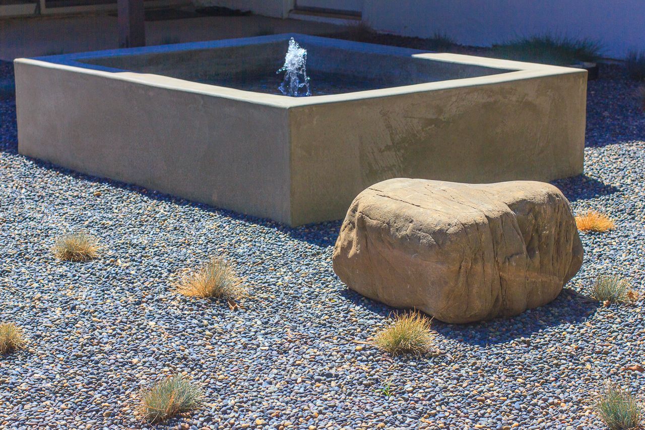 Square concrete fountain with water feature; rock and gravel ground cover.