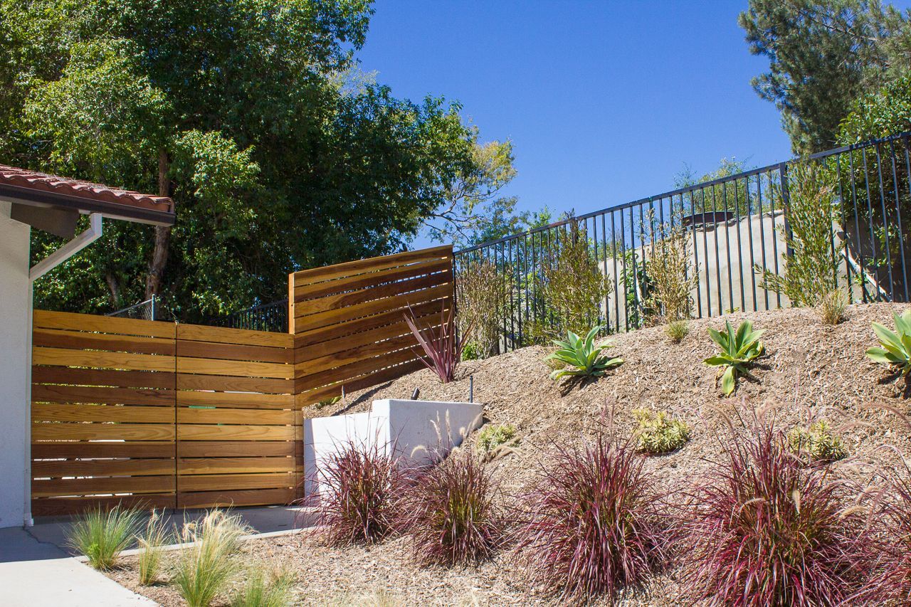 Wooden fence and hillside landscaping under a blue sky.