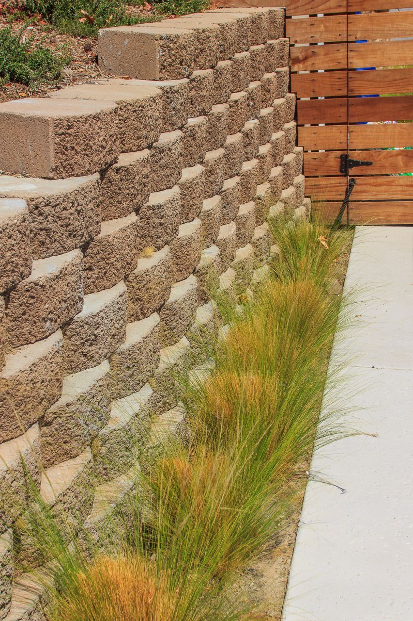 Stone retaining wall with a row of ornamental grass next to a concrete walkway.