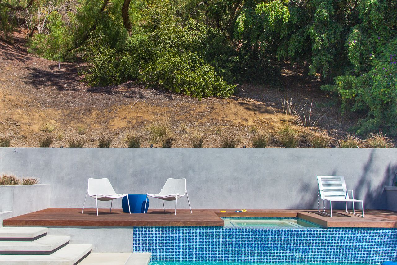 Poolside scene with white chairs, blue accents, and a hillside background.