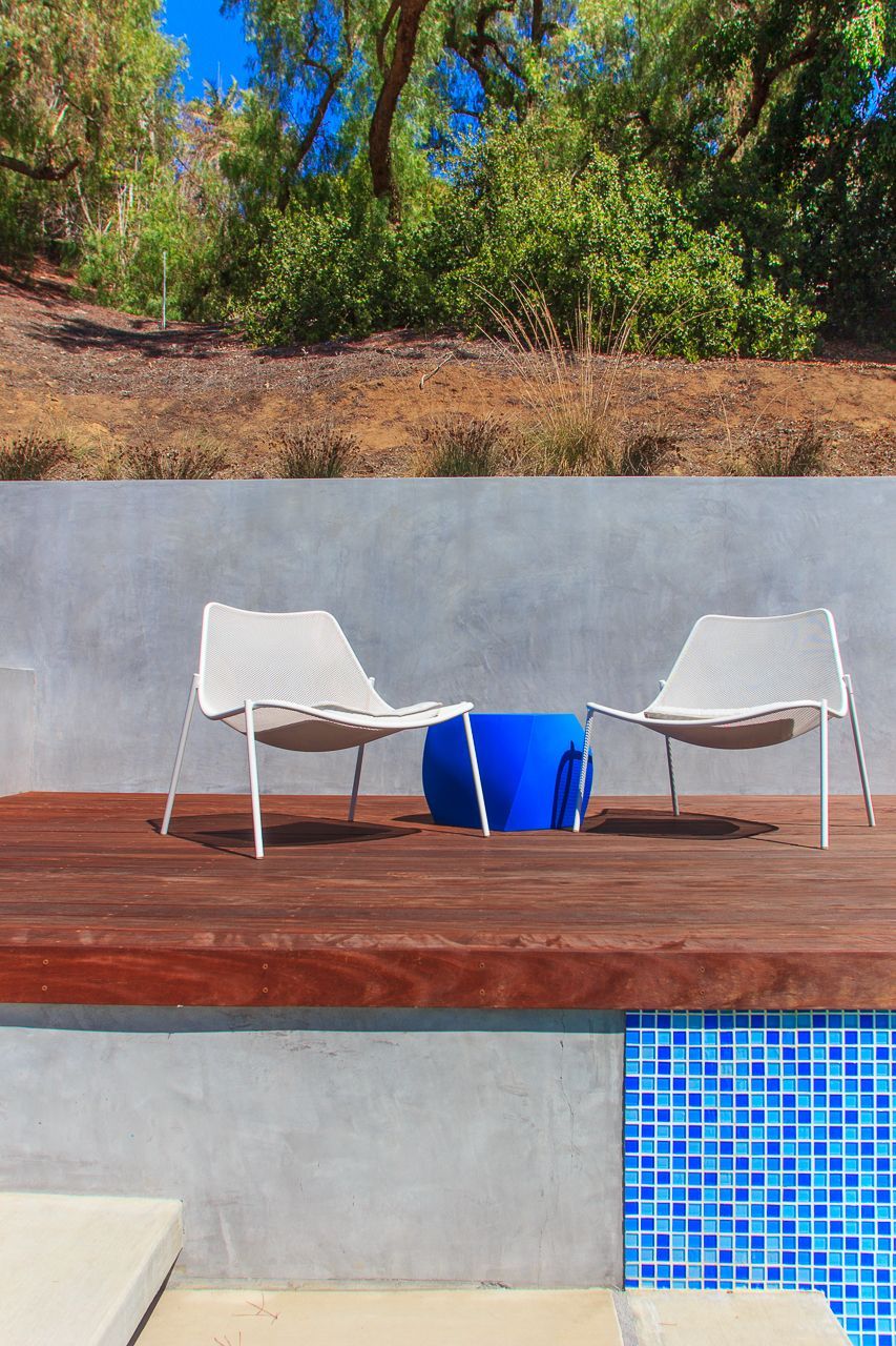 Two white chairs and blue table on a wood deck, overlooking a pool with blue tile.