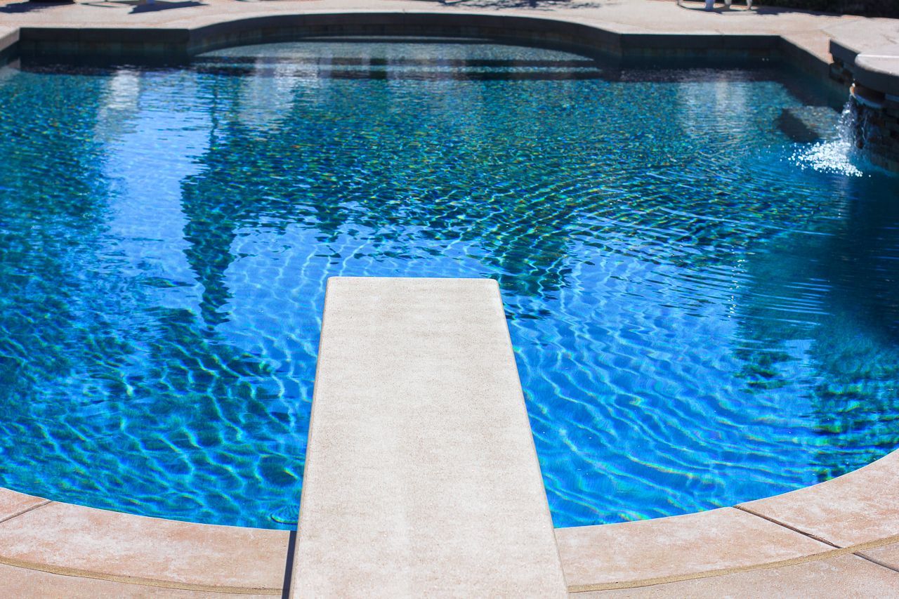 Swimming pool with diving board, blue water, and stone deck.