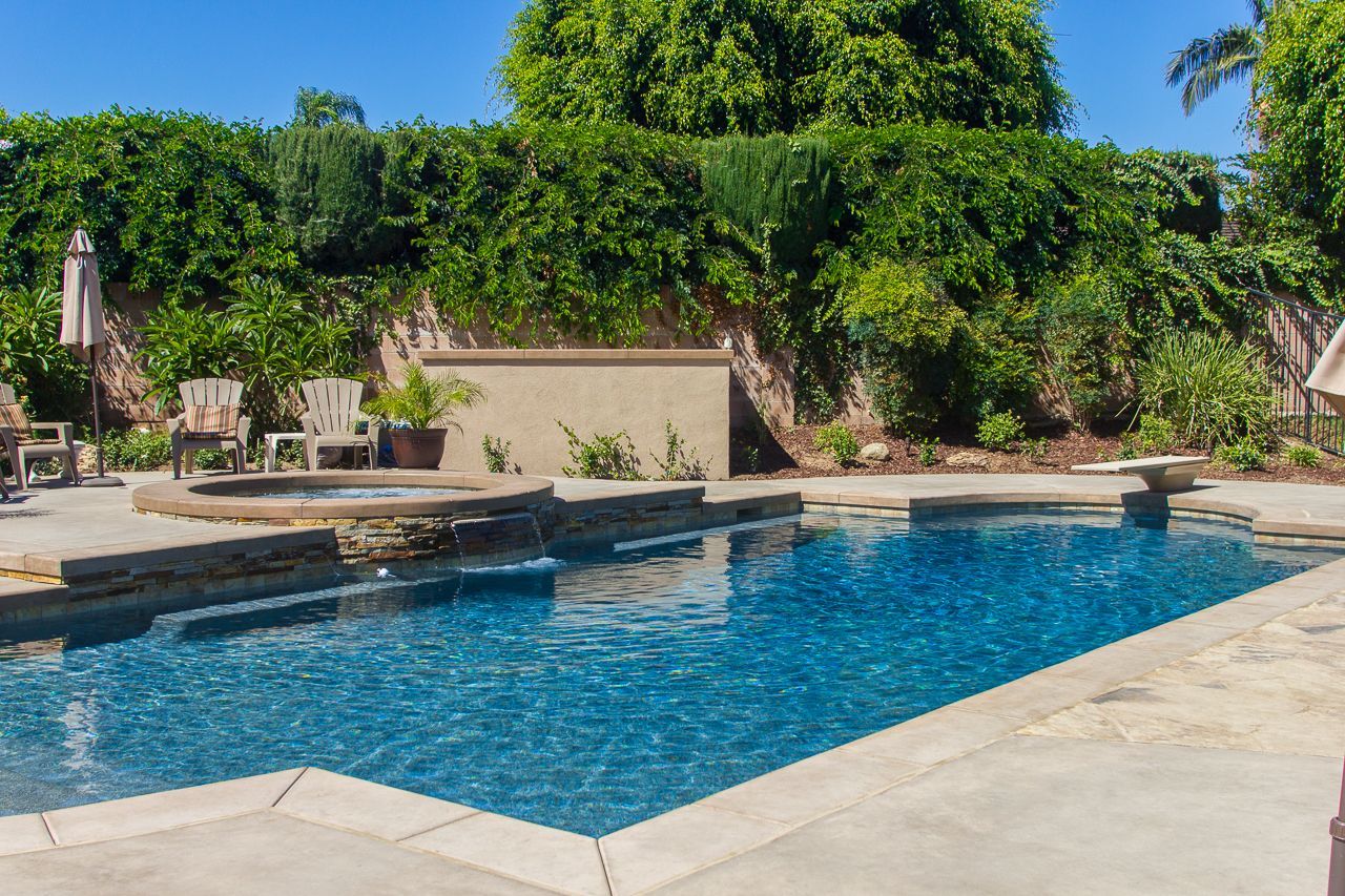 Swimming pool with a stone deck, surrounded by greenery and a wall.