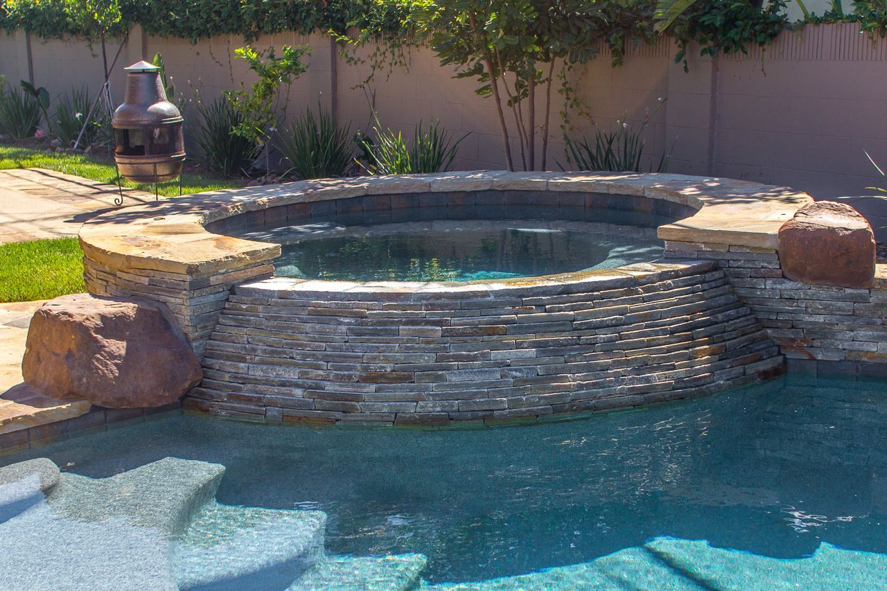 Pool with stone-lined hot tub, waterfall, and steps leading into the blue water.