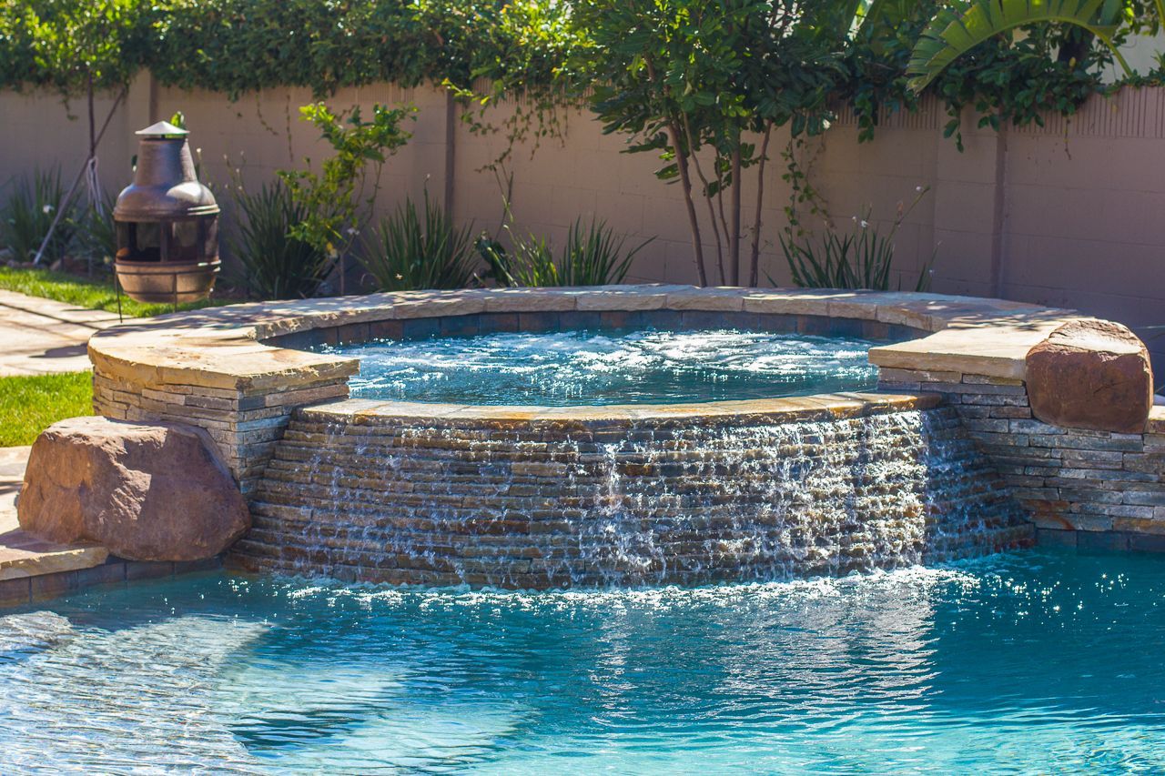 Pool with a cascading waterfall feature, blue water, stone accents, and decorative urn.