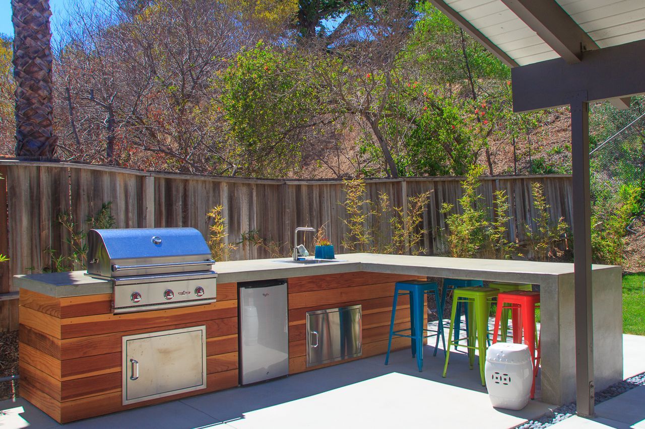 Outdoor kitchen with grill, fridge, and bar seating under a covered patio.