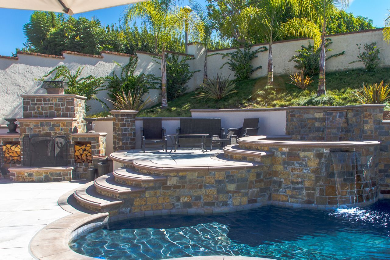 Luxury backyard pool with stone waterfall, fireplace, spa, and seating area.