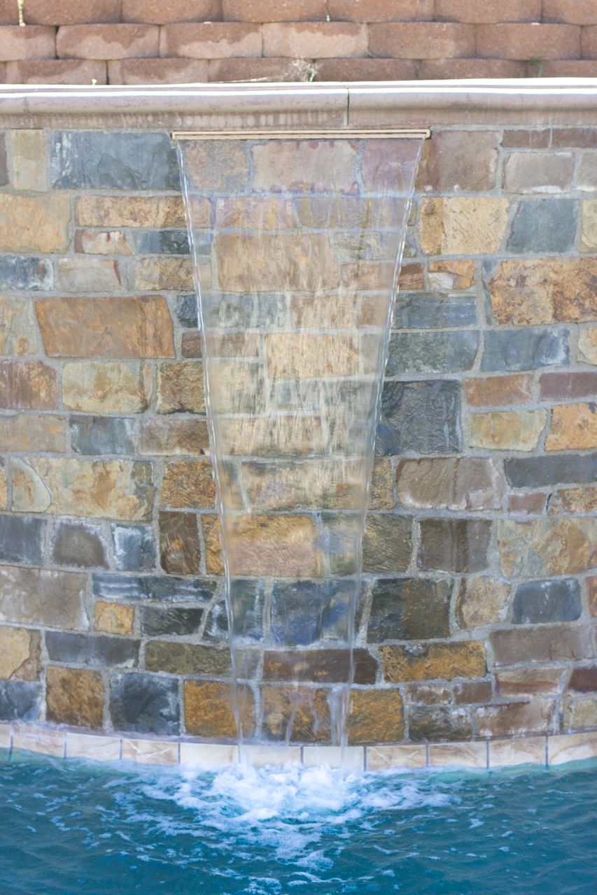 Waterfall cascading into a swimming pool from a stone wall.