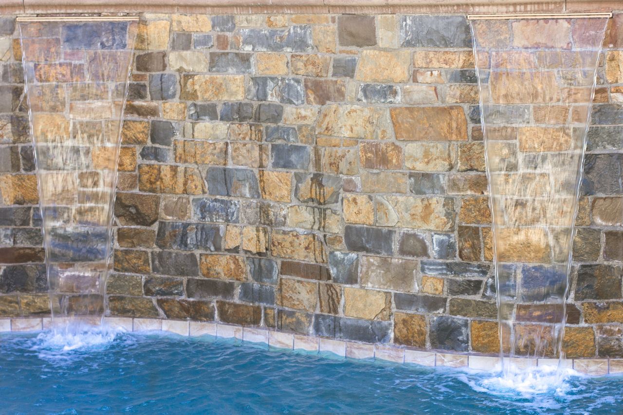Water cascading over a stone wall into a pool of turquoise water.