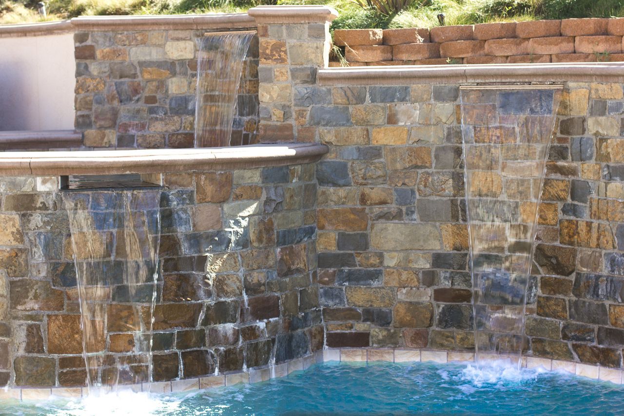 Waterfall feature with water cascading over a stacked stone wall into a swimming pool.