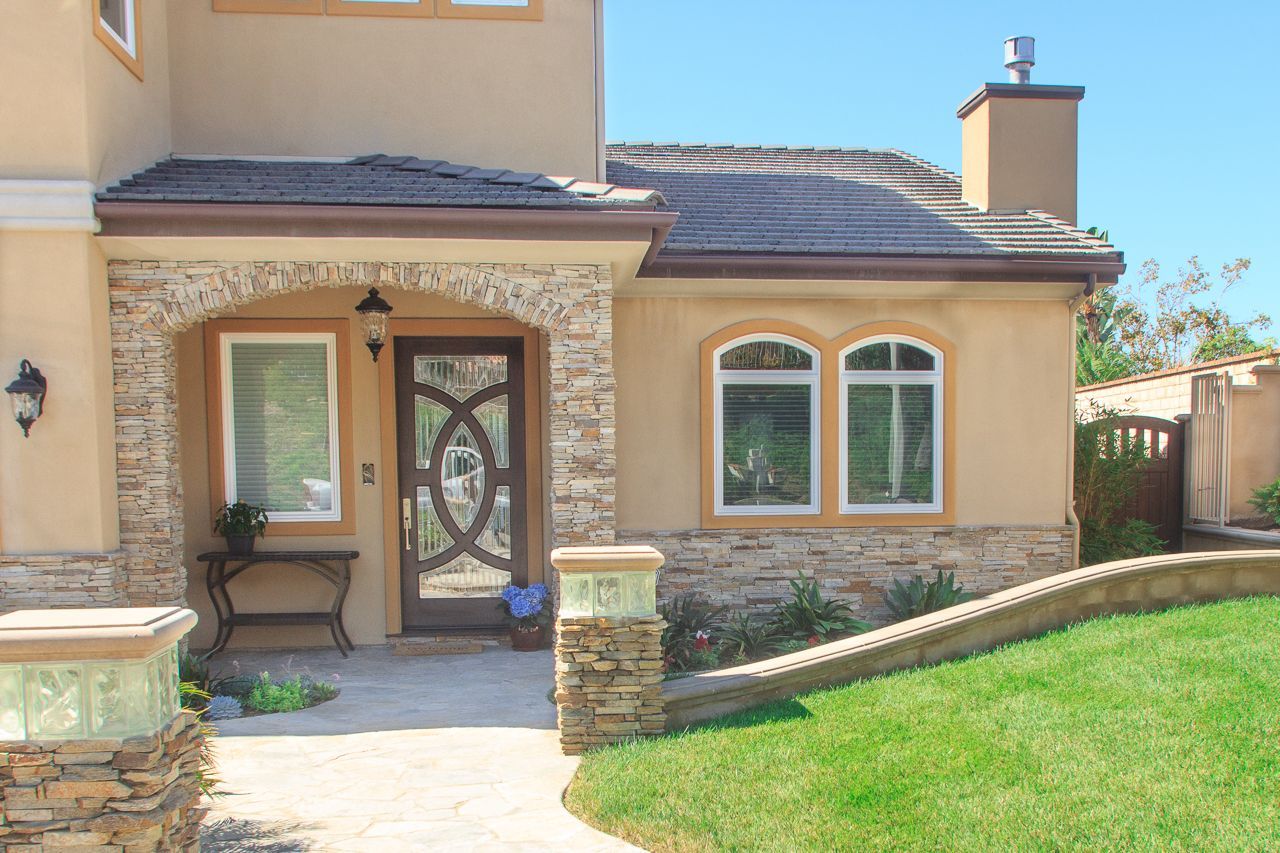 Beige stucco home with stone accents, arched entry and windows, grassy lawn.