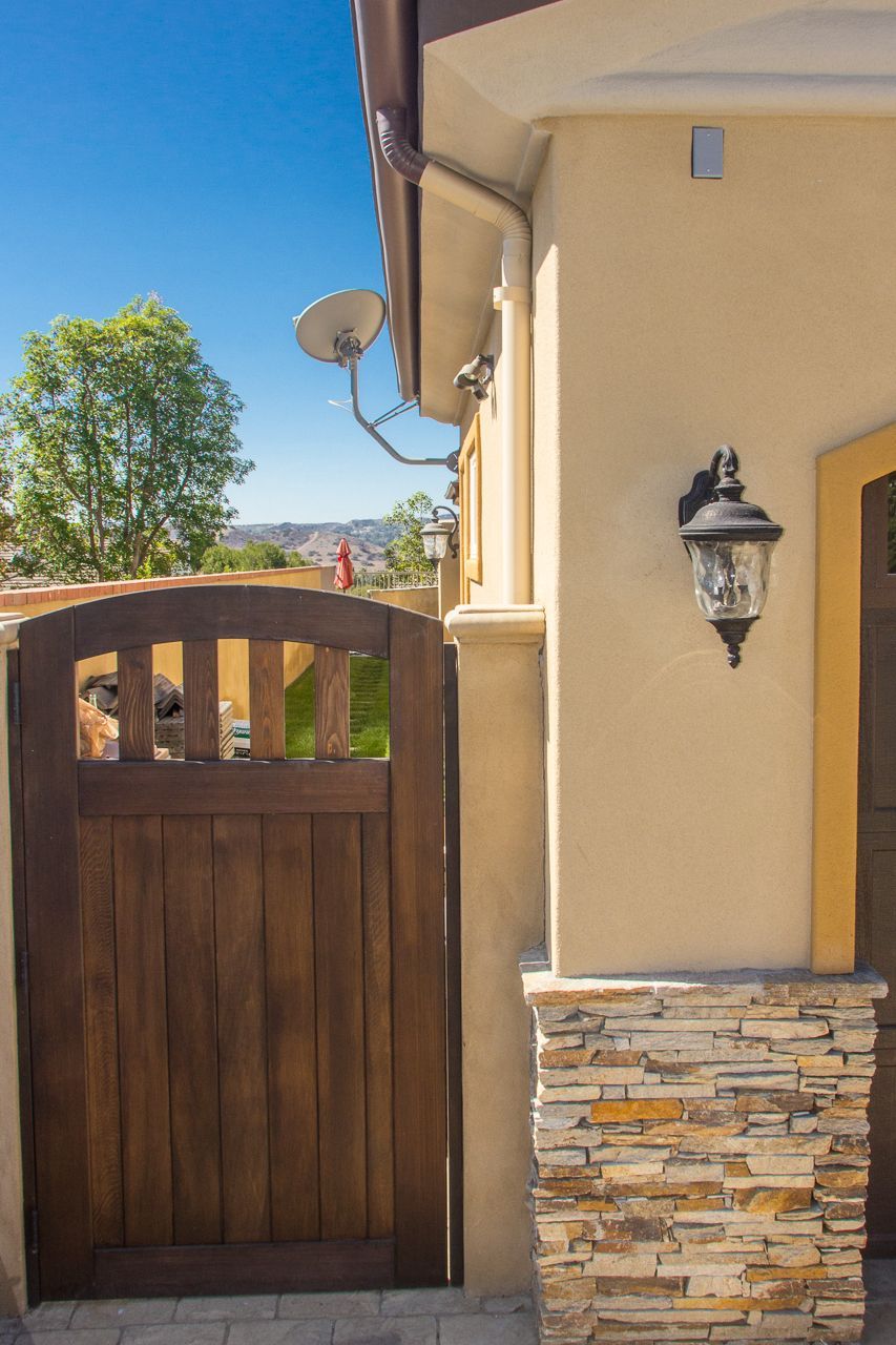 Wooden gate next to a beige stucco wall with a decorative stone base, under a clear blue sky.