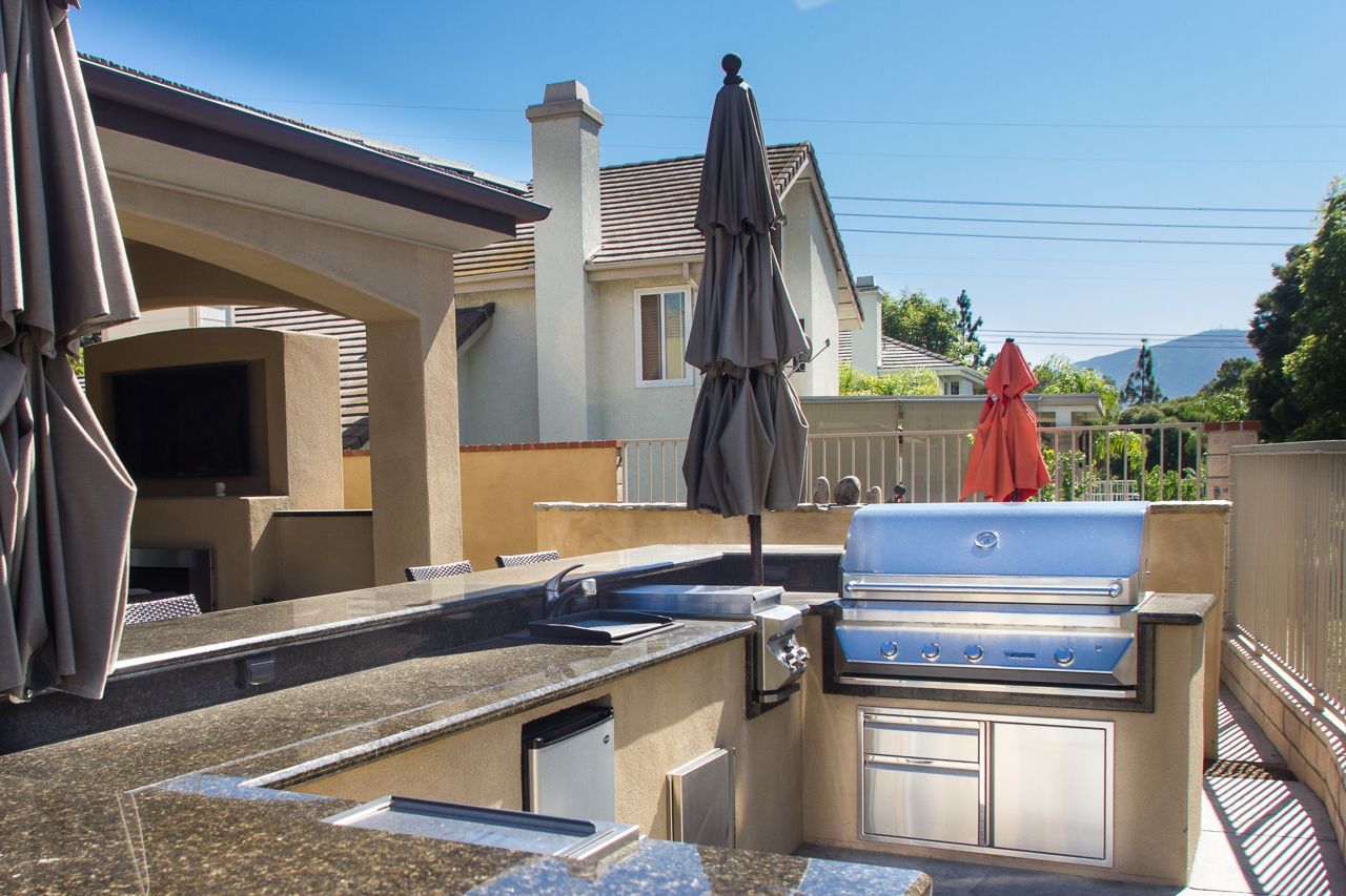Outdoor kitchen with built-in grill, countertops, refrigerator, and umbrellas, on a sunny patio.