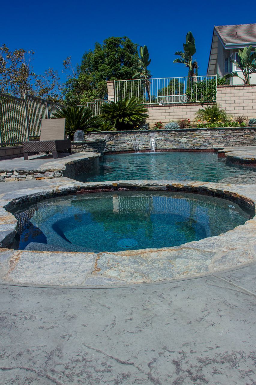 Swimming pool and spa with stone surround, blue water, and backyard setting.