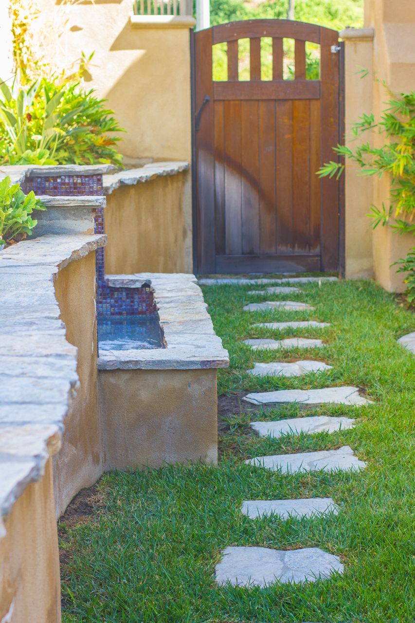 Stone pathway leading to a wooden gate, flanked by a low wall and grass.