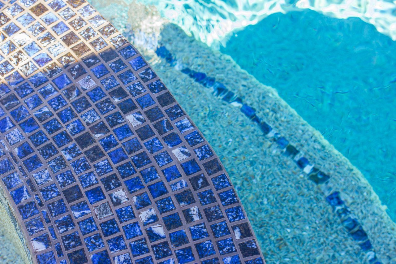 Close-up of a pool's edge, showing blue tile and clear water.