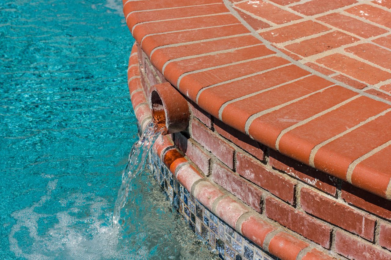 Brickwork edge of pool with water cascading through openings.