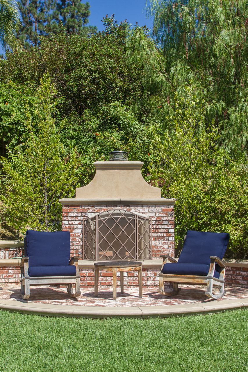 Outdoor seating area with fireplace, two blue cushioned chairs, and small table.