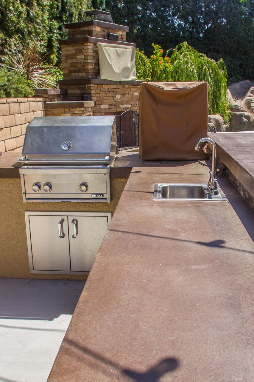 Outdoor kitchen with stainless steel grill, sink, and brown countertop.