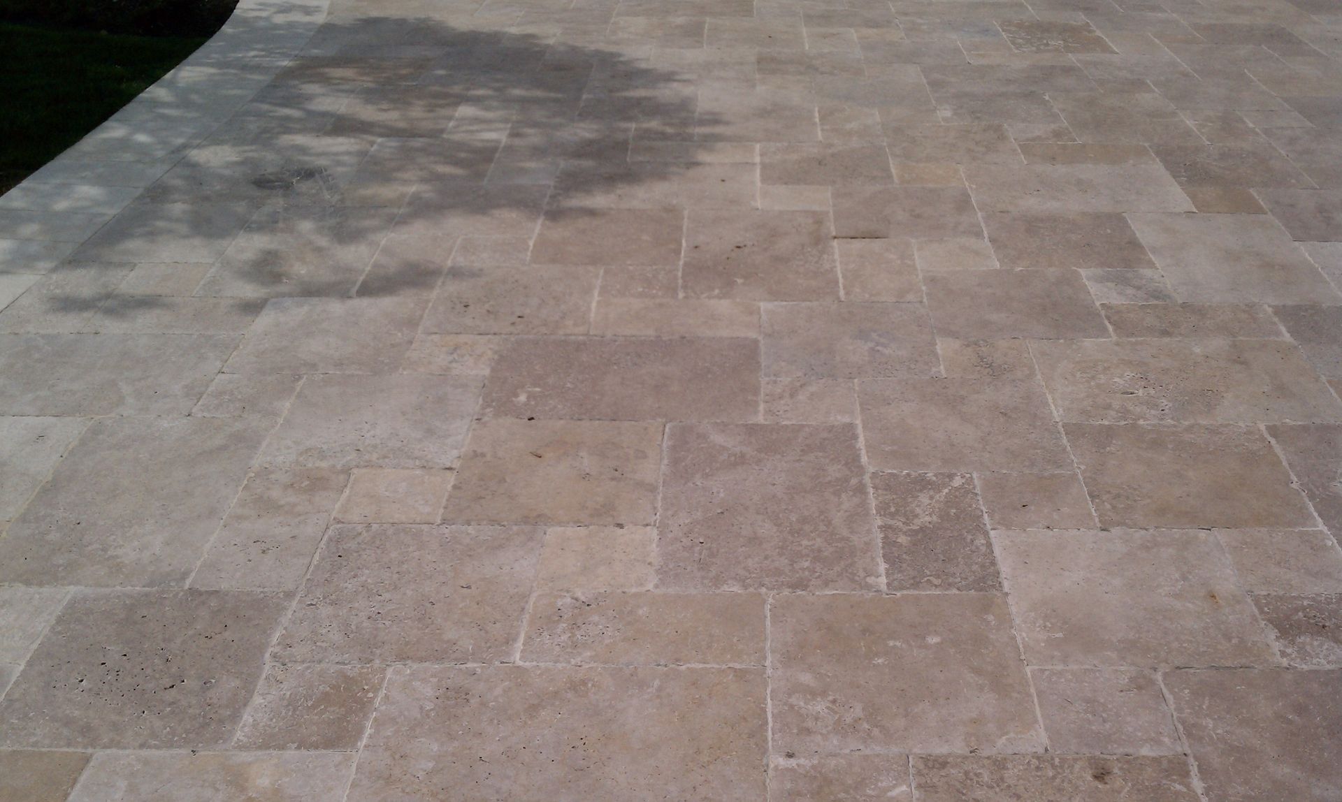 Beige rectangular stone tile patio with tree shadow.