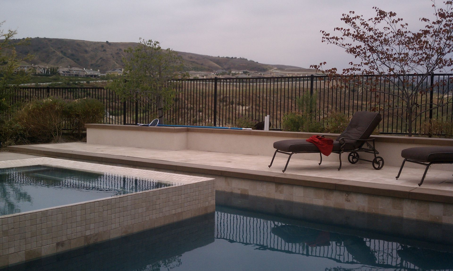 Poolside scene with pool, lounge chairs, and distant hills under overcast sky.