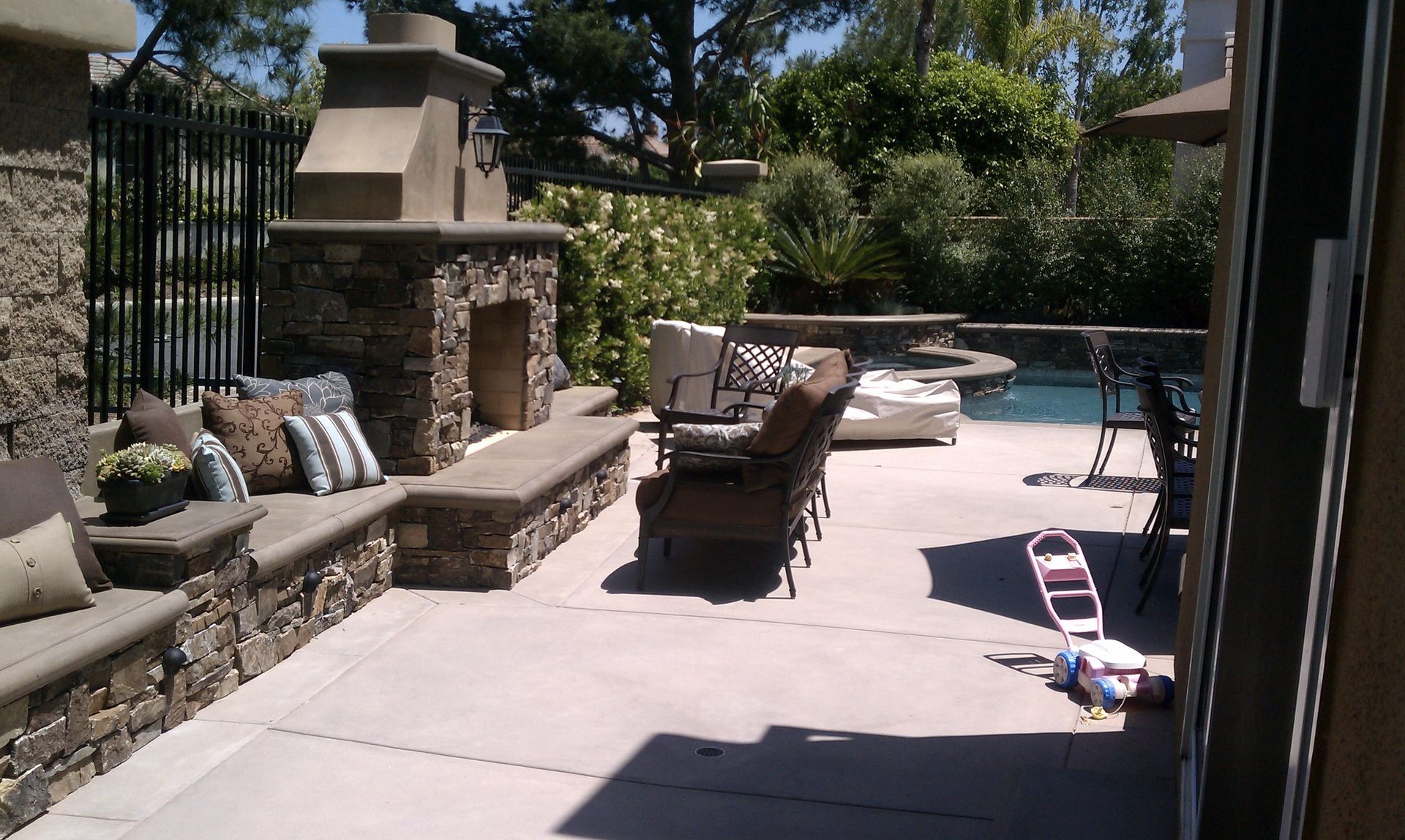 Patio with stone fireplace and seating, overlooking a pool.