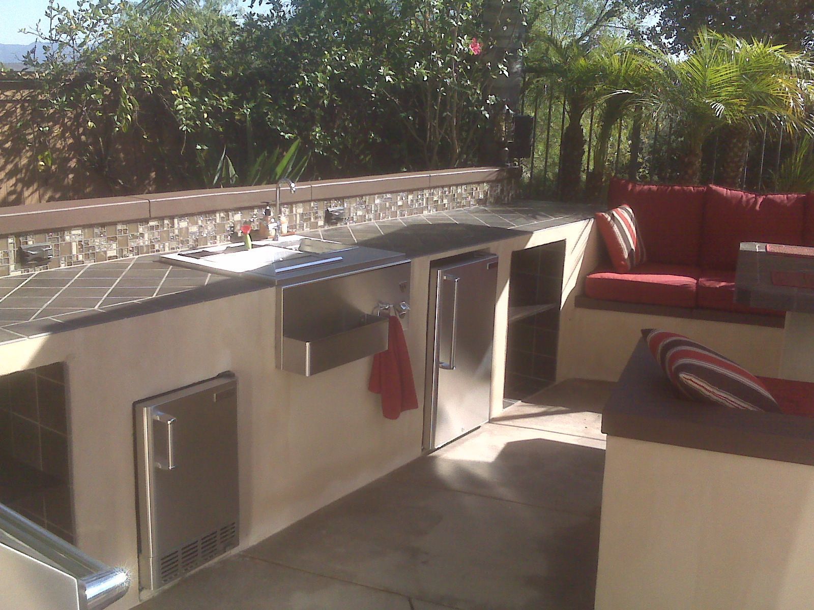 Outdoor kitchen with stainless steel appliances, sink, and red cushioned seating.