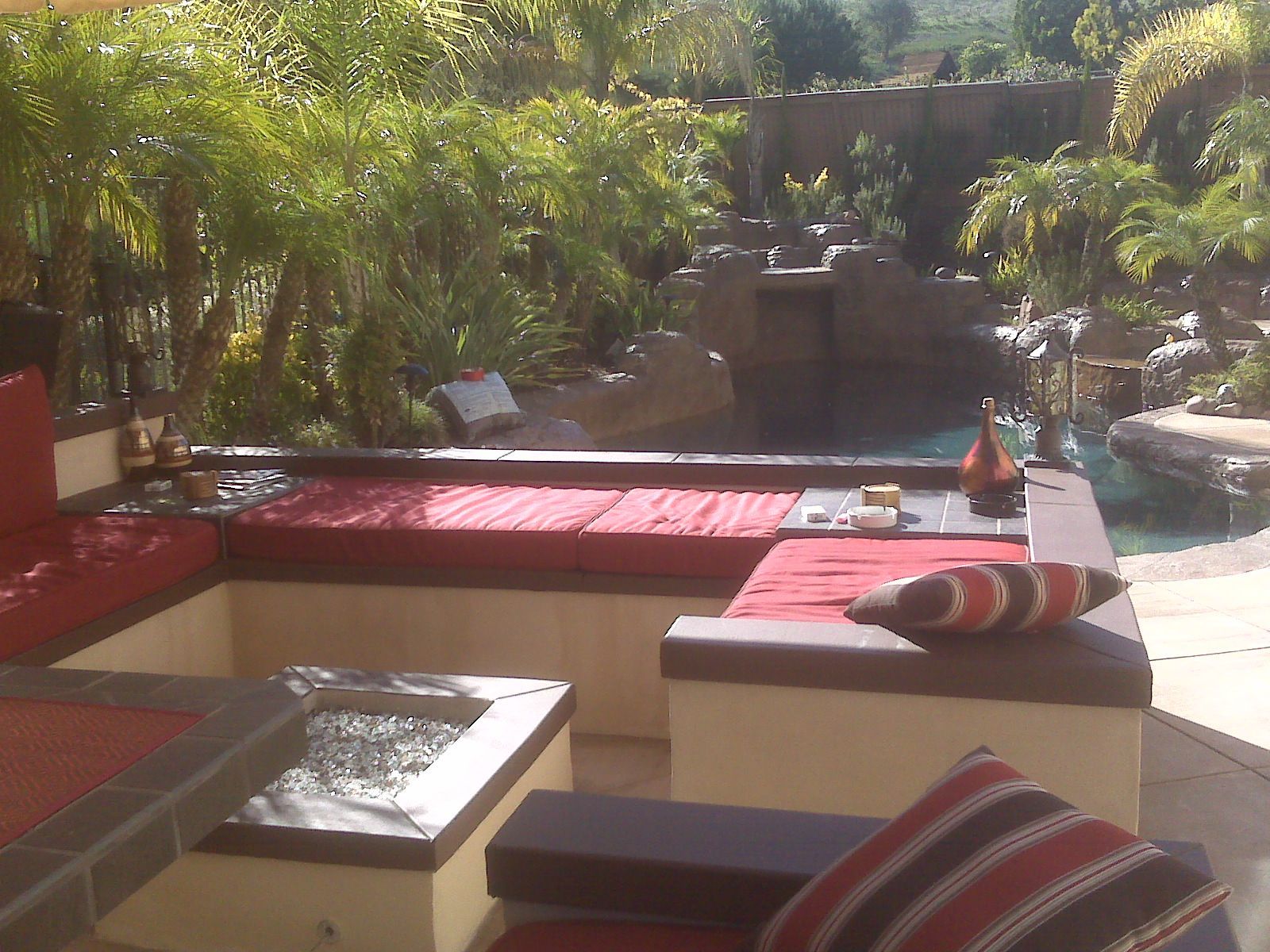 Outdoor patio with built-in seating, cushions, and a water feature in a lush garden setting.
