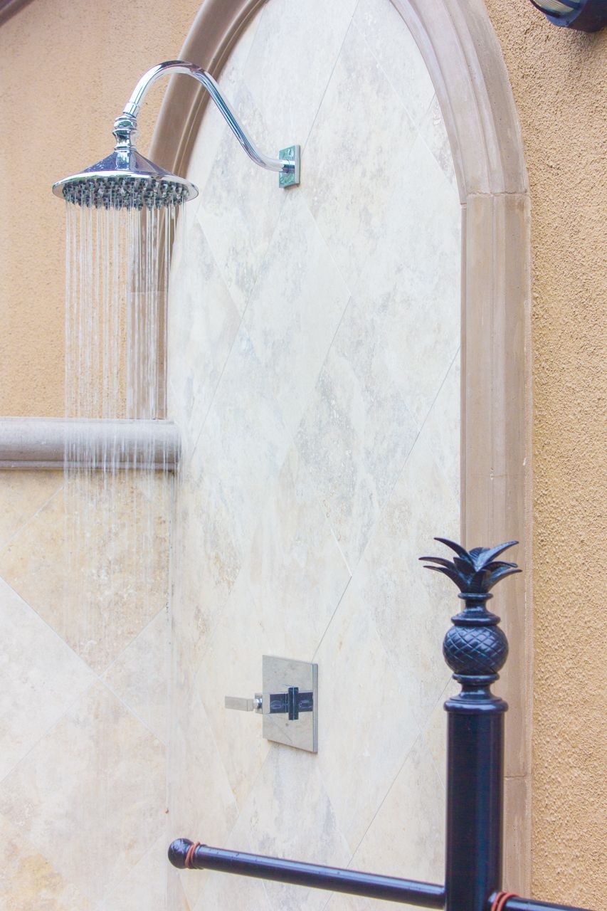 Outdoor shower with silver fixtures, water flowing, set against a stucco wall with arched trim.
