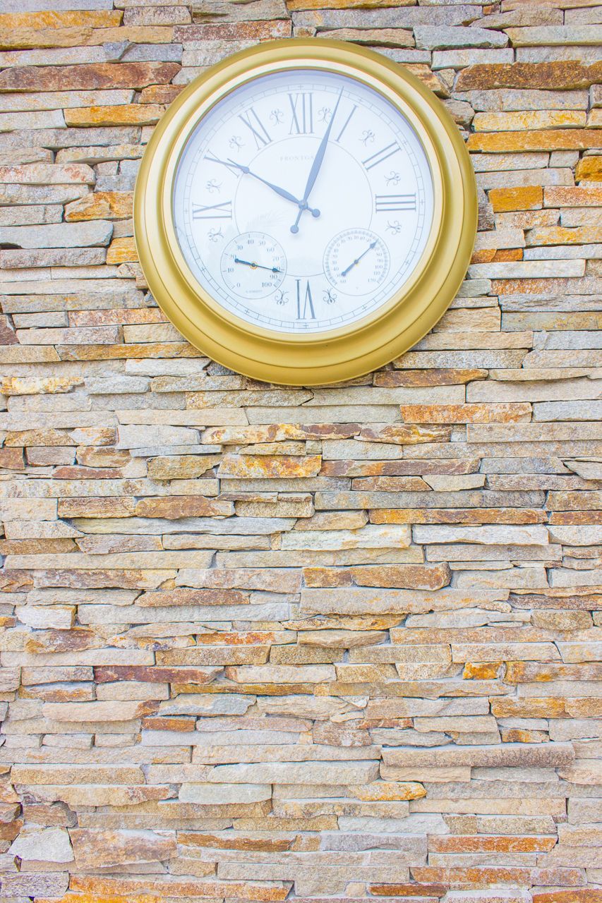 Gold-framed clock with three small dials mounted on a multi-colored stone wall.
