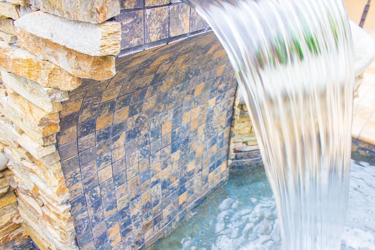 Waterfall cascading over a stone wall into a pool.