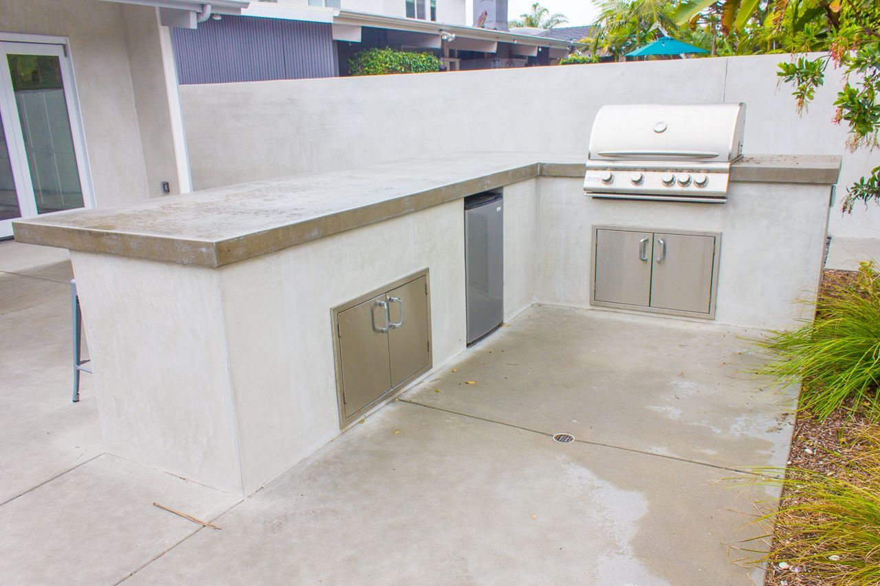 Outdoor kitchen with concrete countertop, stainless steel grill, and storage cabinets.