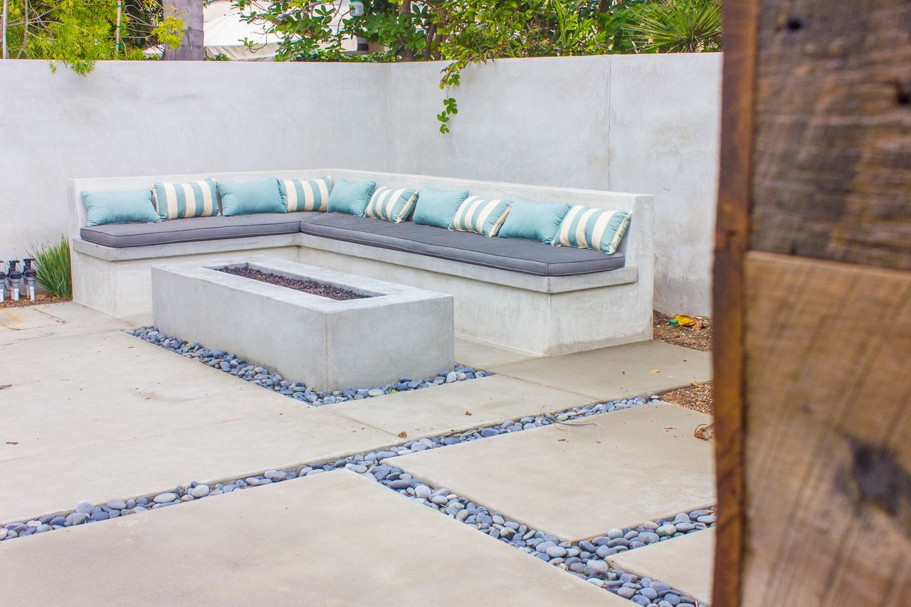 Concrete patio with built-in bench, fire pit, blue cushions, and stone accents.