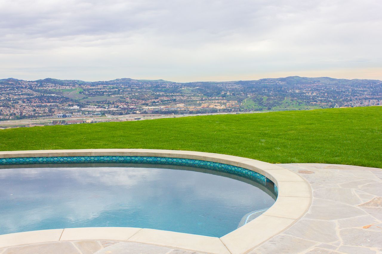 Pool with blue water and stone edge overlooking city and cloudy sky.