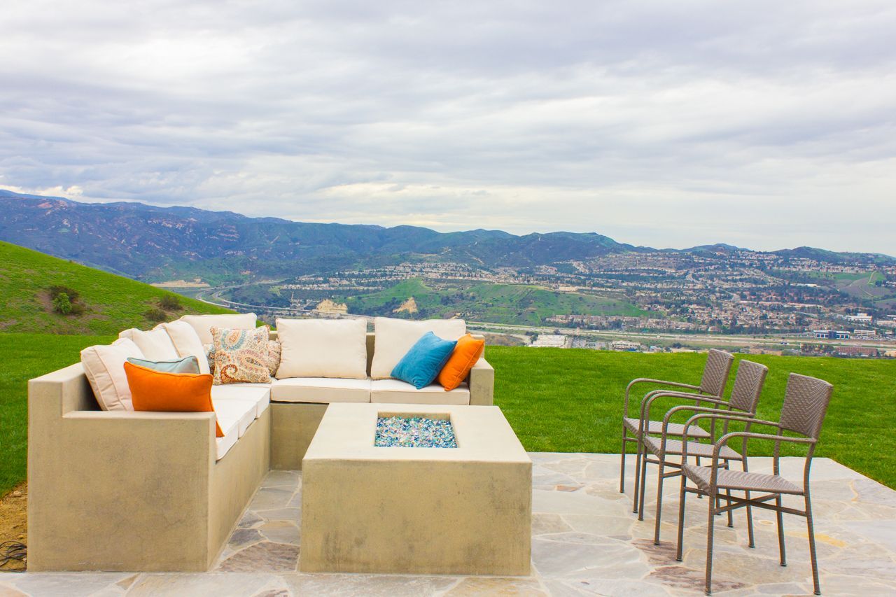 Outdoor patio with sectional sofa, fire pit, chairs, green lawn, and city view.