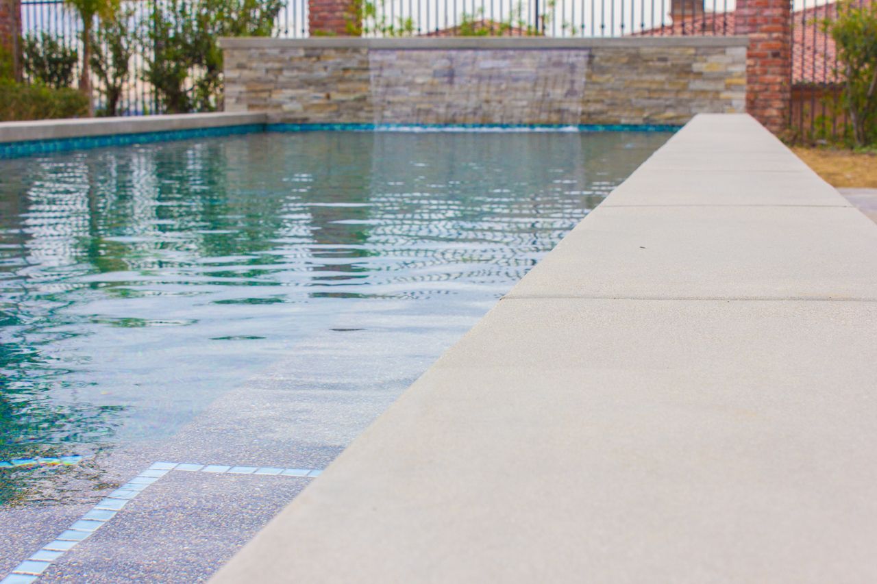 Swimming pool with beige coping, waterfall feature, and clear water.