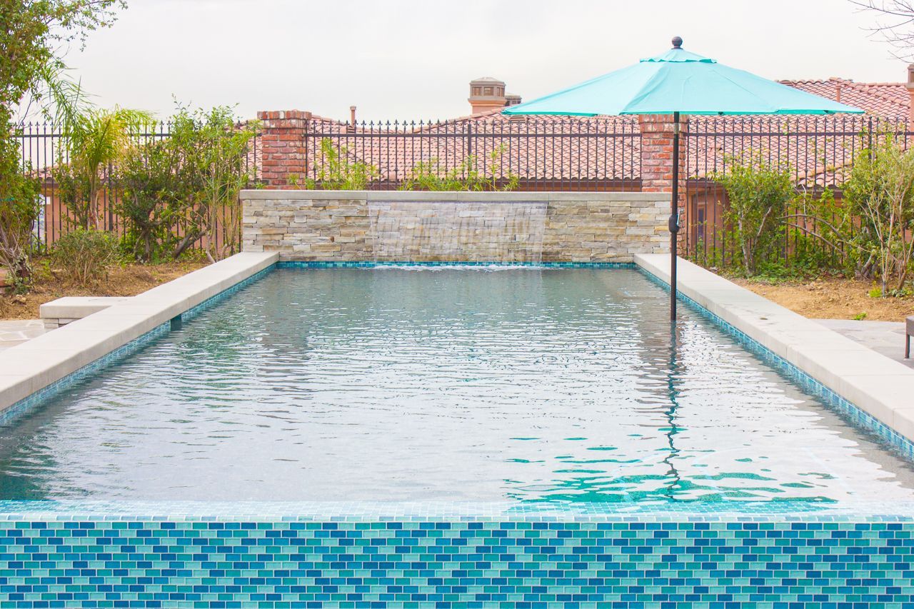 Rectangular pool with turquoise tile, a waterfall feature, and a teal umbrella.