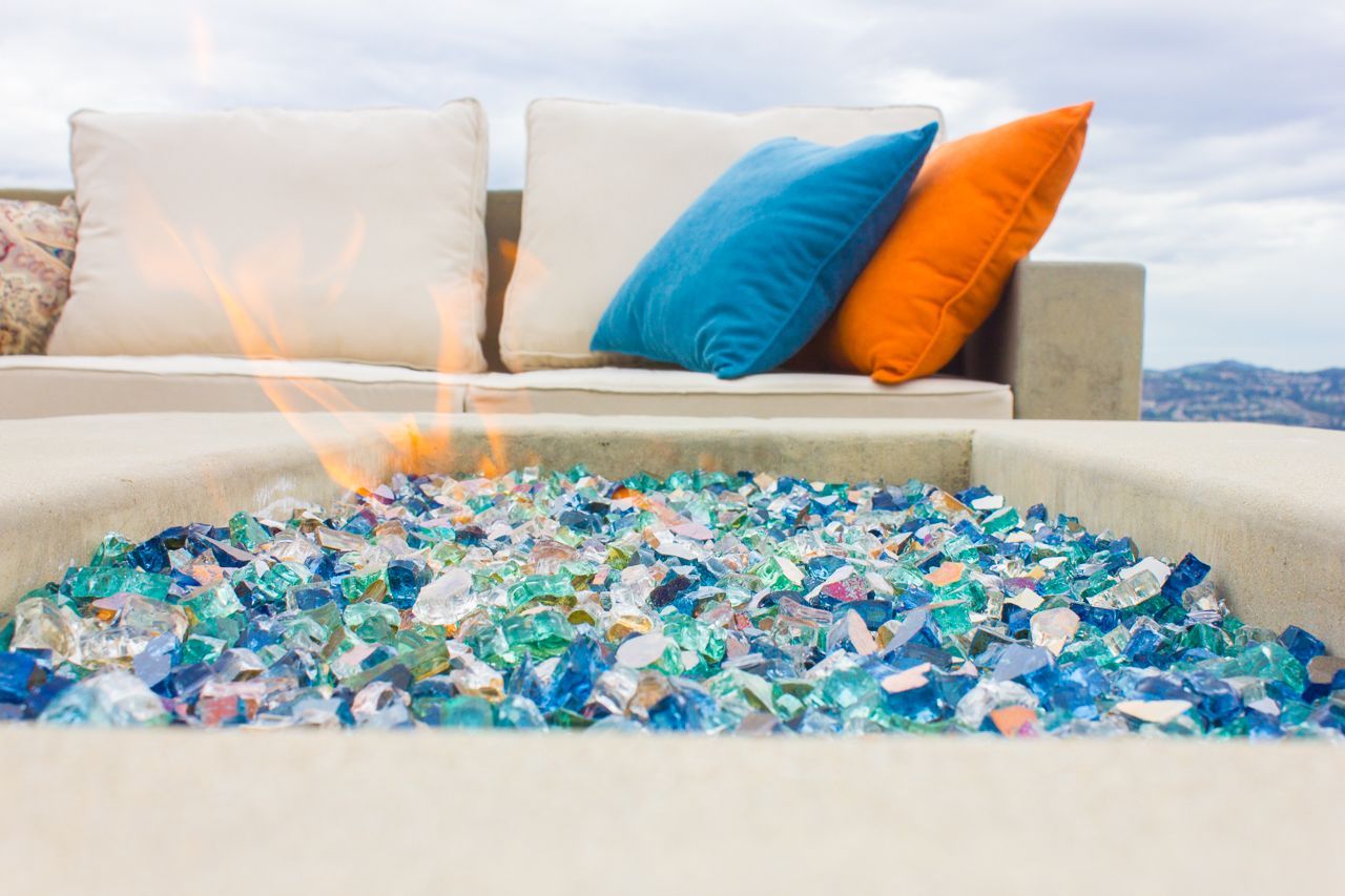 Fire pit with blue and orange cushions, colorful glass. Outdoor setting.